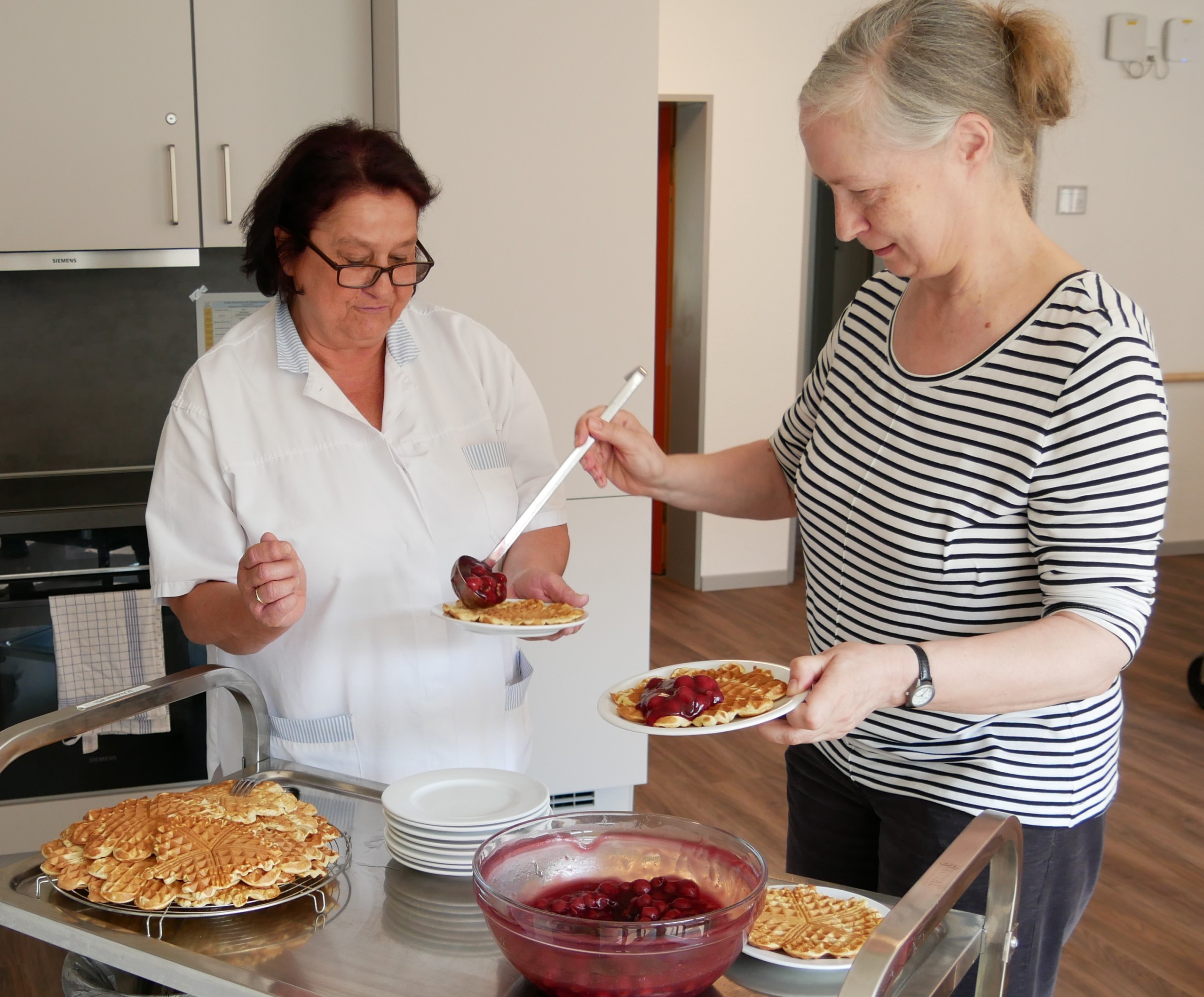 Zwei Frauen bereiten Teller mit Waffeln und Kirschen vor