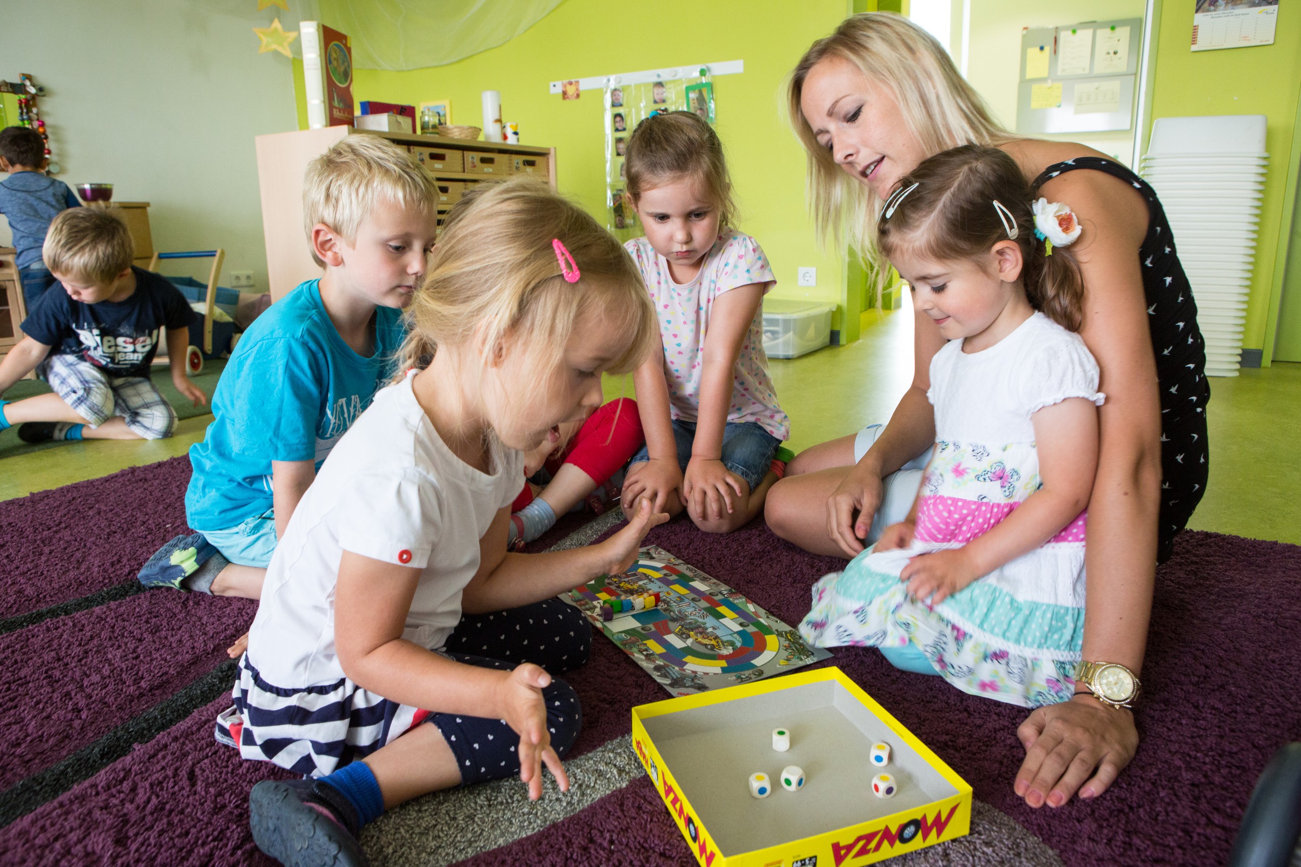 Mehrere Kinder spielen mit einer erwachsenen Person auf dem Boden sitzend ein Würfelspiel