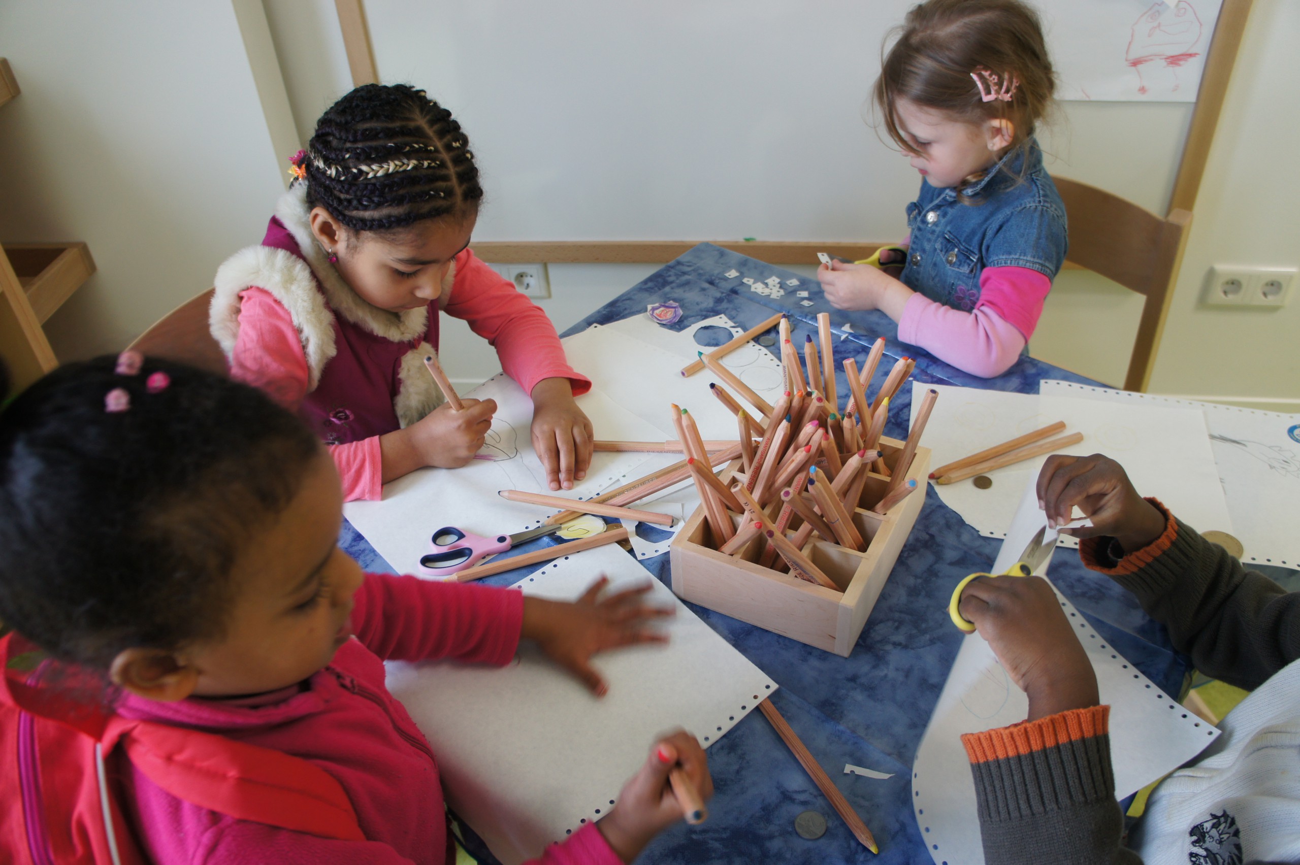 Mehrere Kinder sitzen malend an einem Tisch mit vielen Buntstiften und Papier