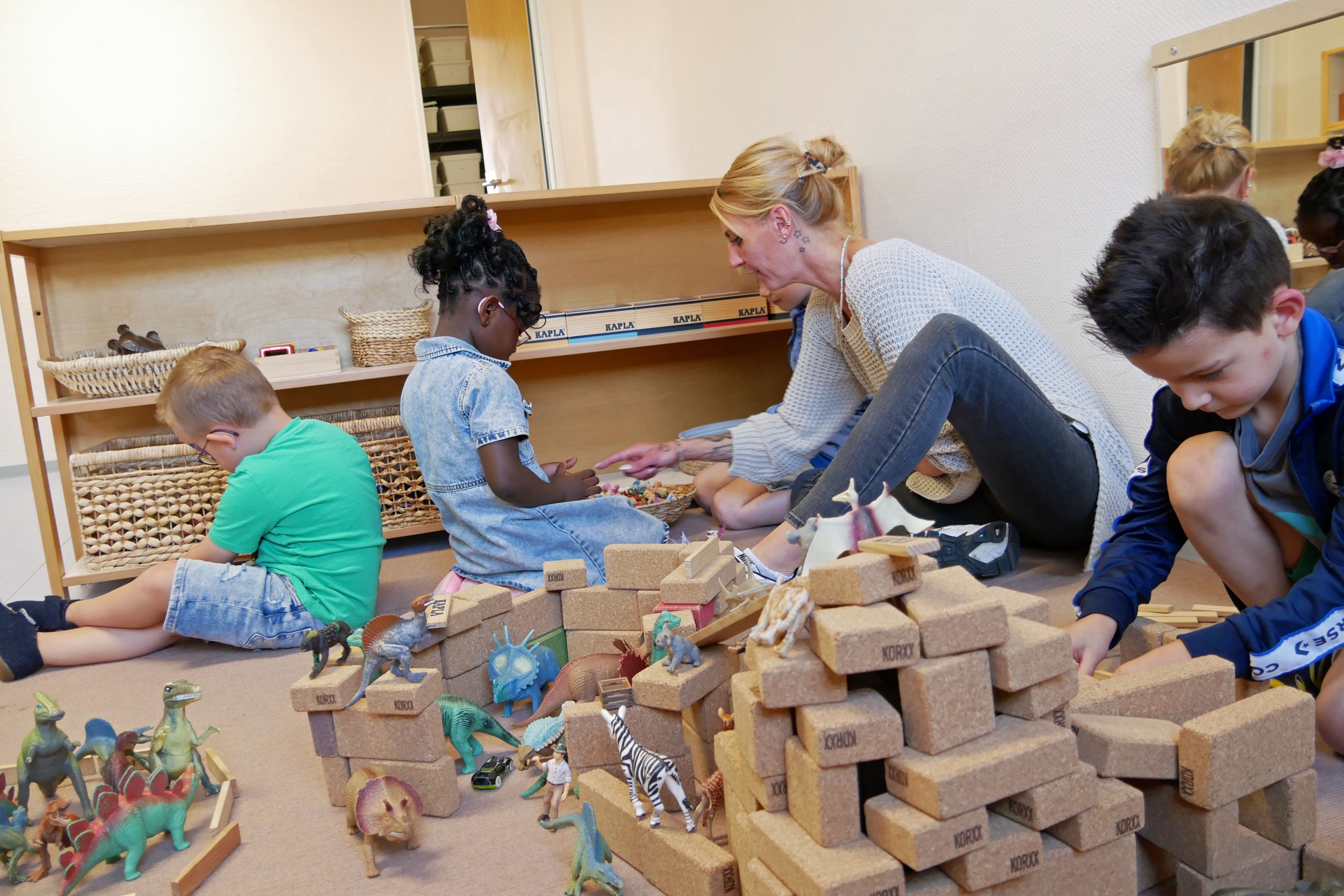 Drei Kinder und eine erwachsene Person spielen in einer Bauecke