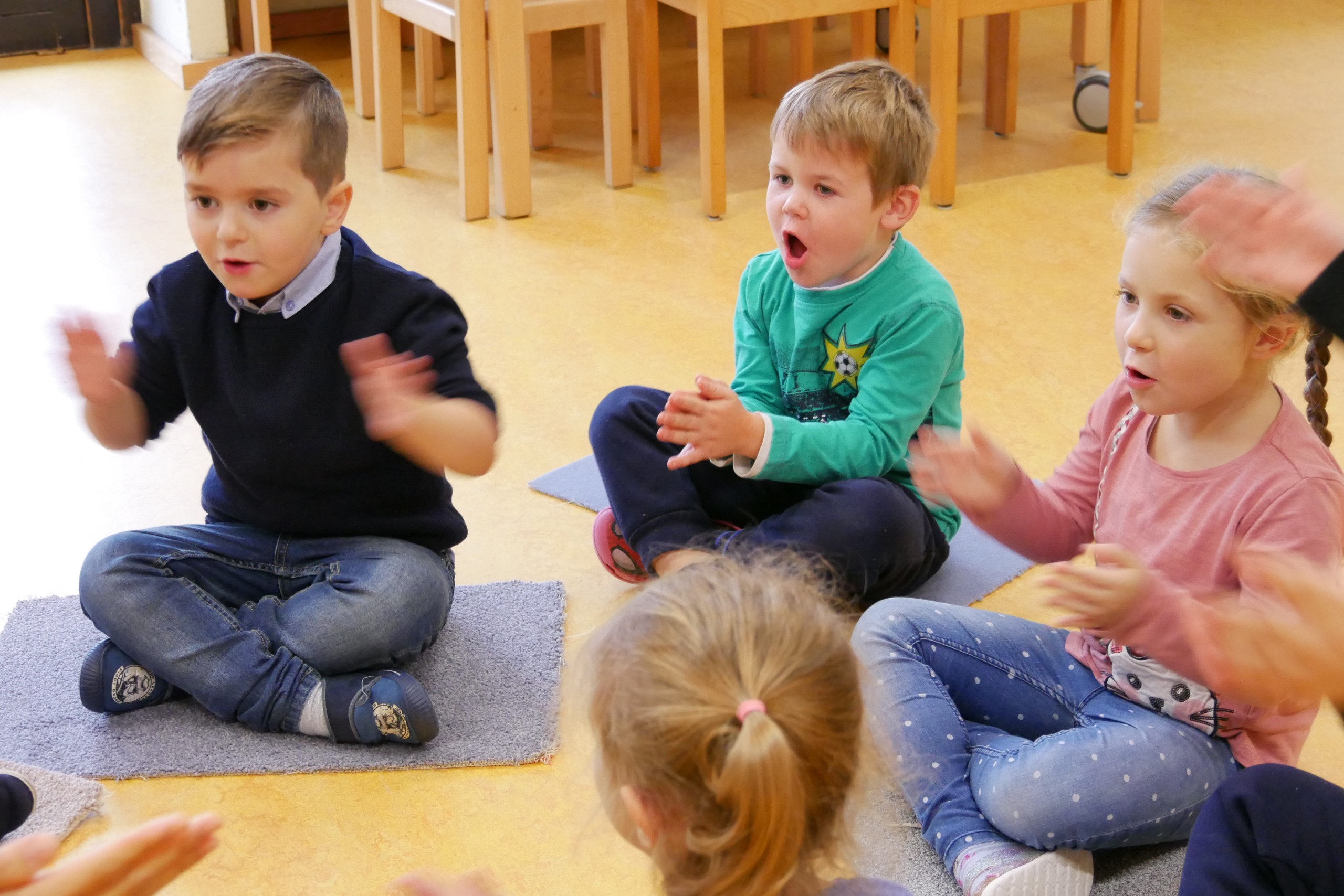 Kinder sitzen singend und klatschend im Kreis