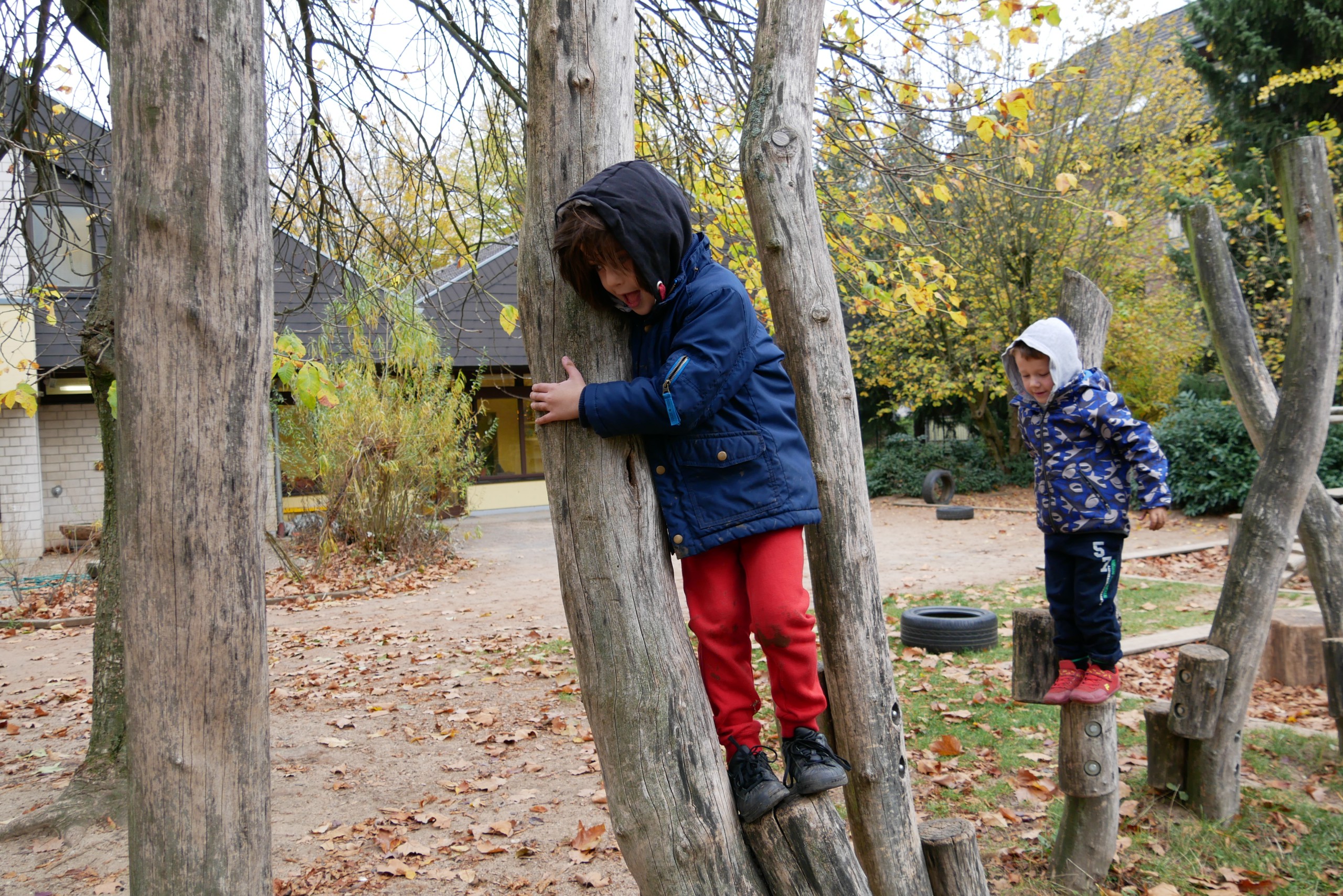 Zwei Kinder klettern auf Baumstämmen im Außengelände