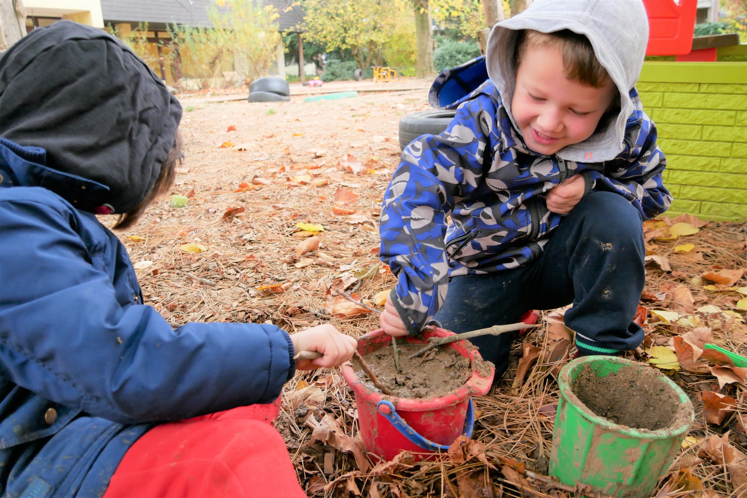 Zwei Kinder spielen draußen mit Eimern und Erde