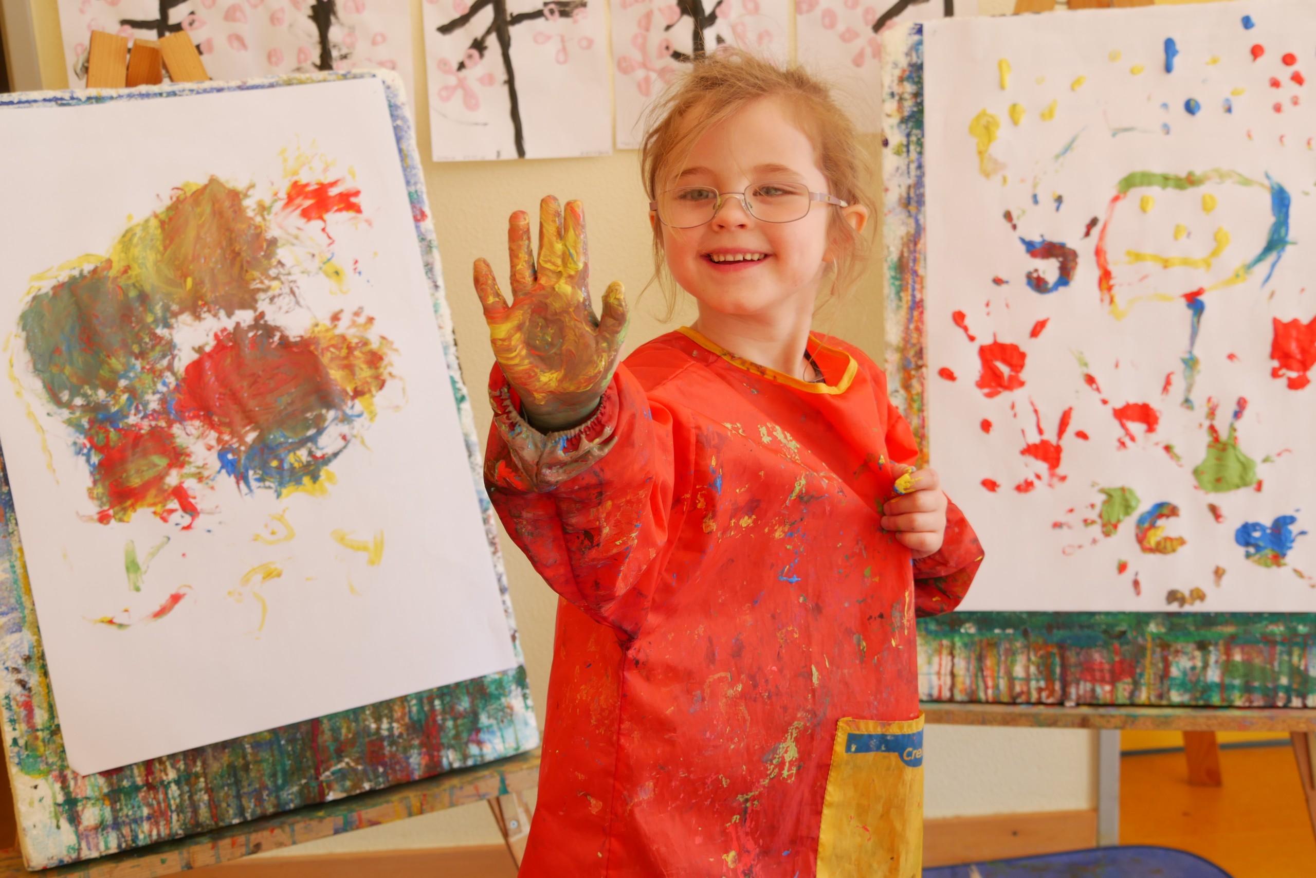 Kind zeigt seine von Fingerfarben bunte Hand in die Kamera