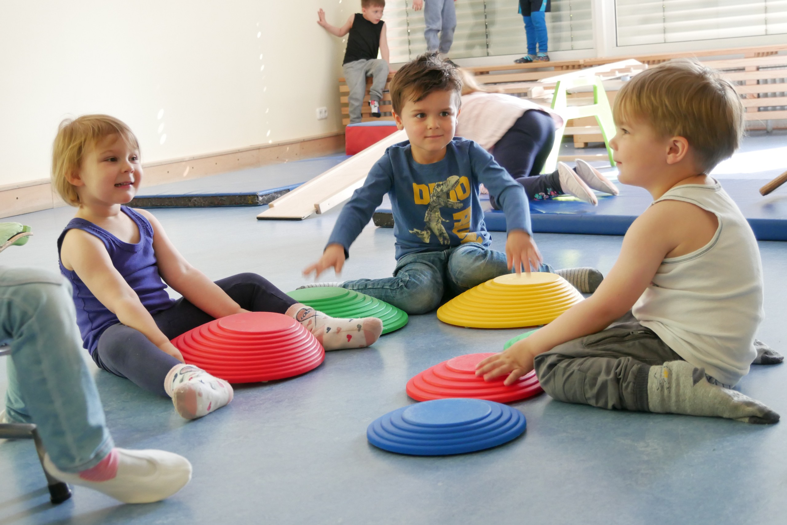 Drei Kinder sitzen in der Turnhalle auf dem Boden im Kreis und spielen