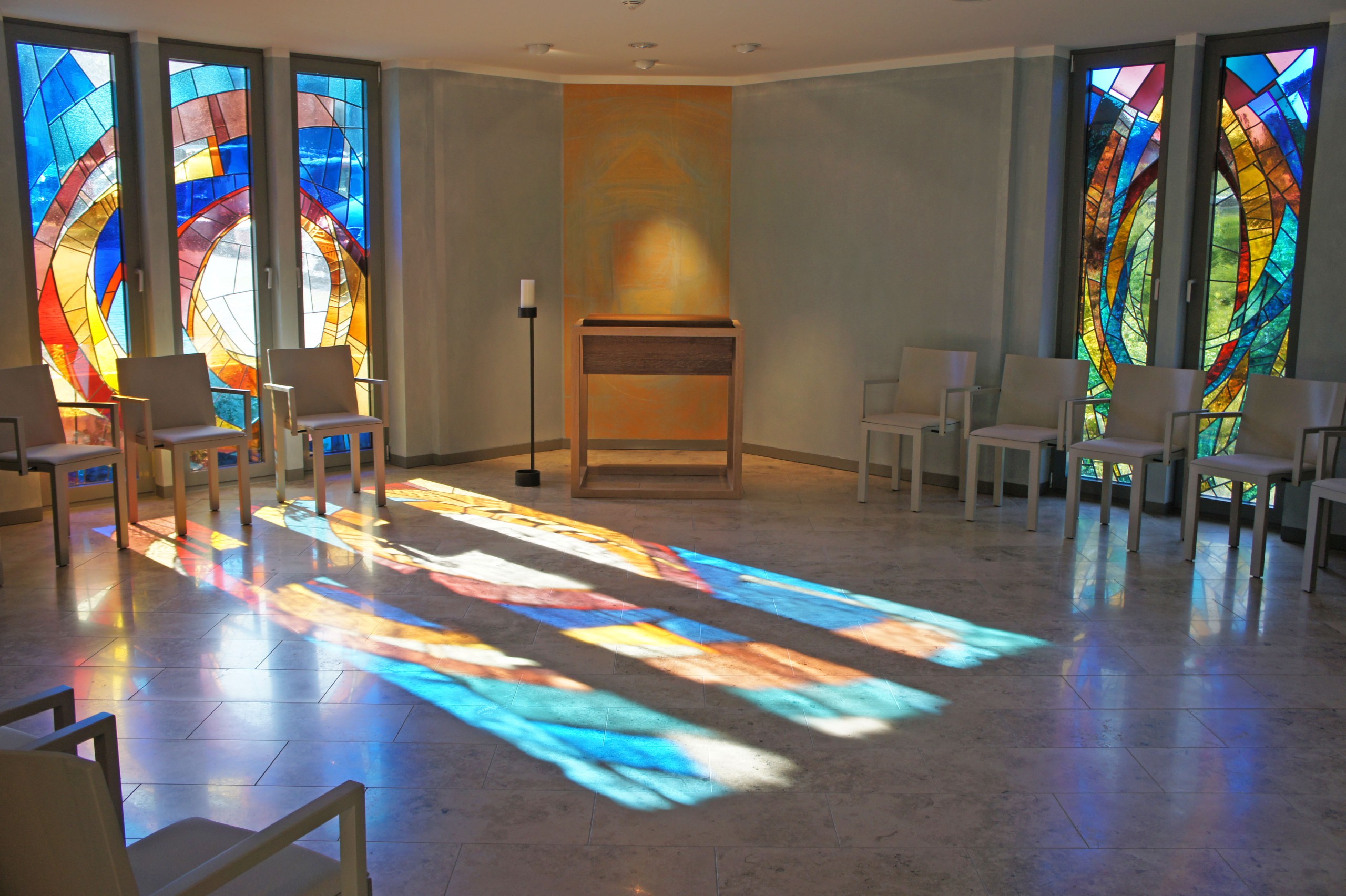 Andachtsraum mit bunten Fenstern, Stuhlkreis und Altar